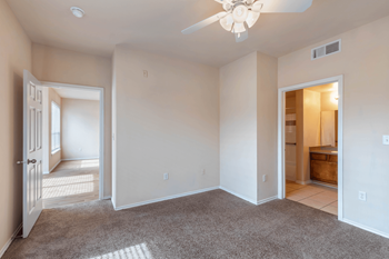 a bedroom with a doorway to the bathroom. Plush carpeting and a ceiling fan.
